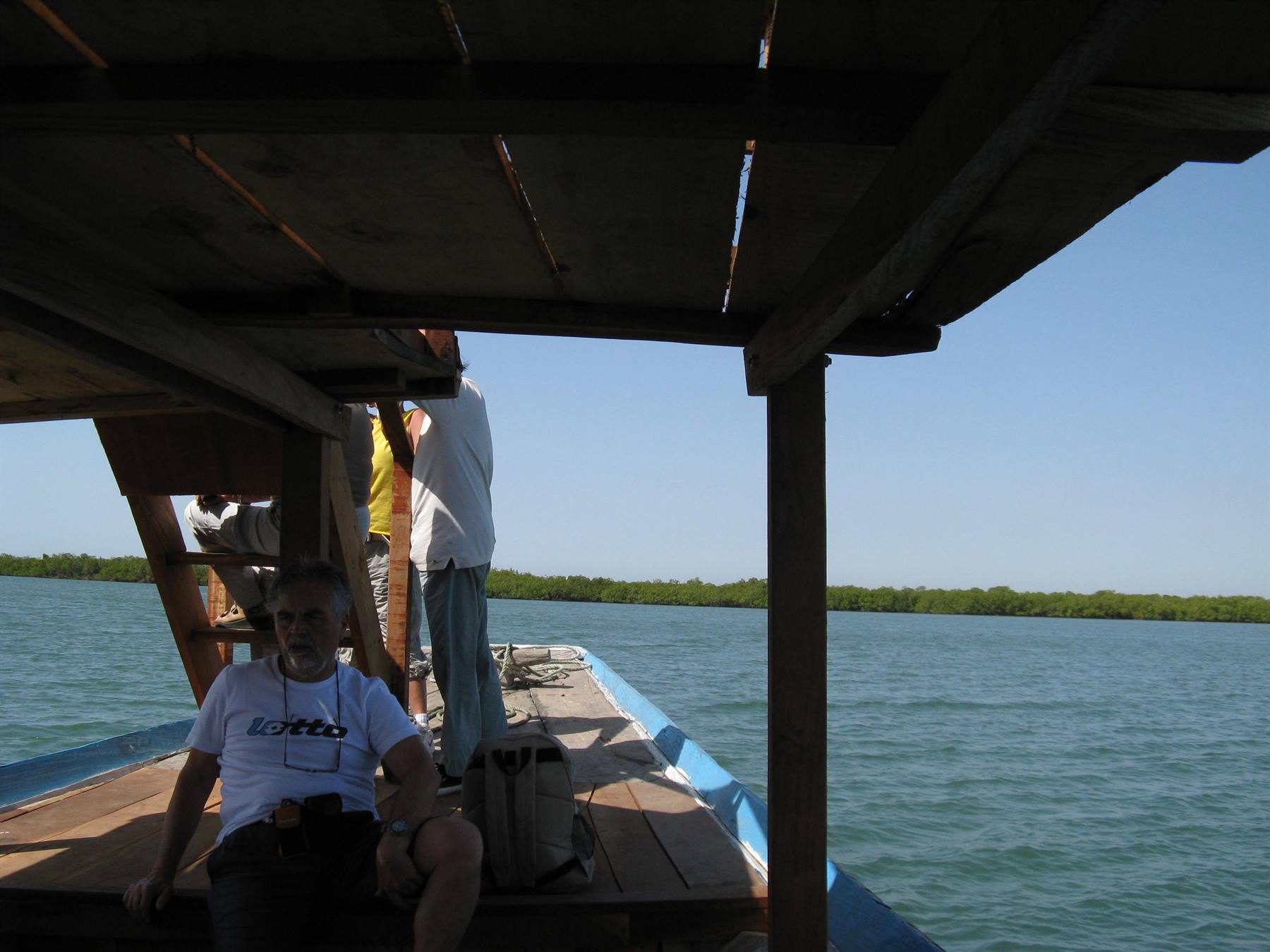 Tourists on wooden covered boat, blue water and green shoreline
