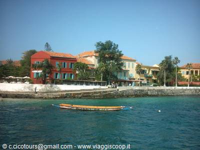 Colorful boat on turquoise water in front of colonial buildings and trees