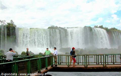 Tourists on metal walkway in front of Iguazú Falls, mist and greenery