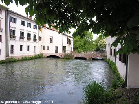 Buranelli canal in Treviso, stone bridge between pale facades and leafy trees