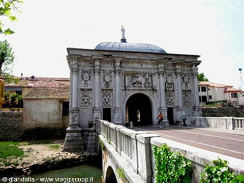 Cyclists crossing Porta San Tomaso, old stone gate with bridge over the river