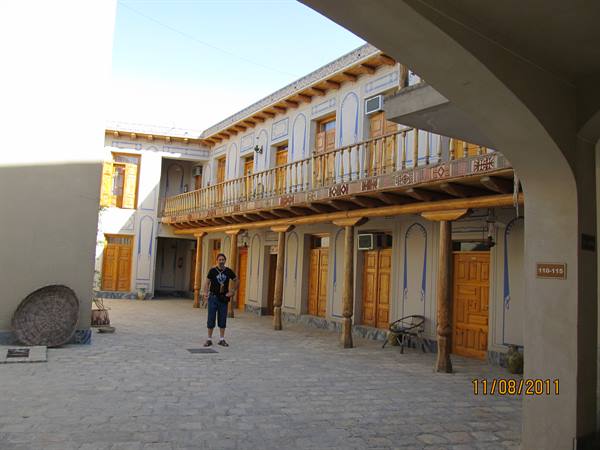 Tourist in traditional courtyard with wooden balcony and carved doors, Bukhara