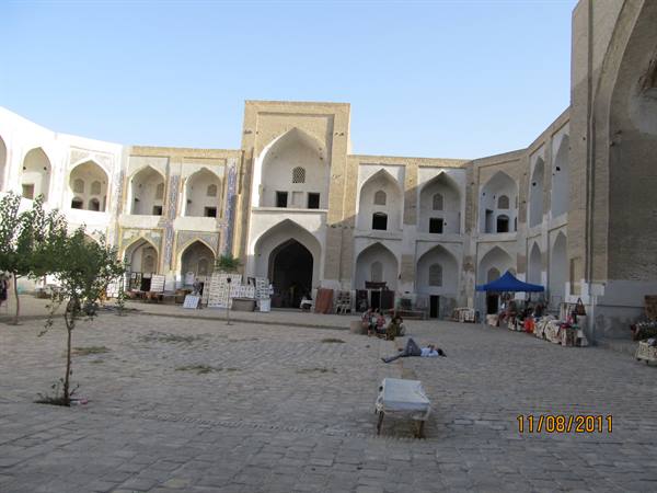 Madrasa courtyard in Bukhara, brick arches and souvenir stalls under blue sky