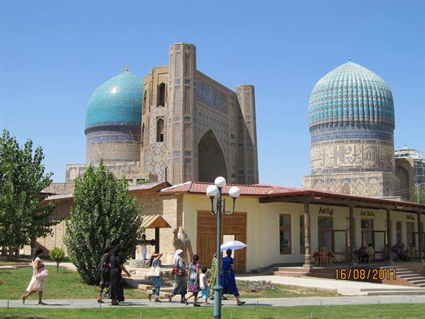 Tourists walk past Bibi-Khanum Mosque in Samarkand, blue domes and tiles under sunny sky