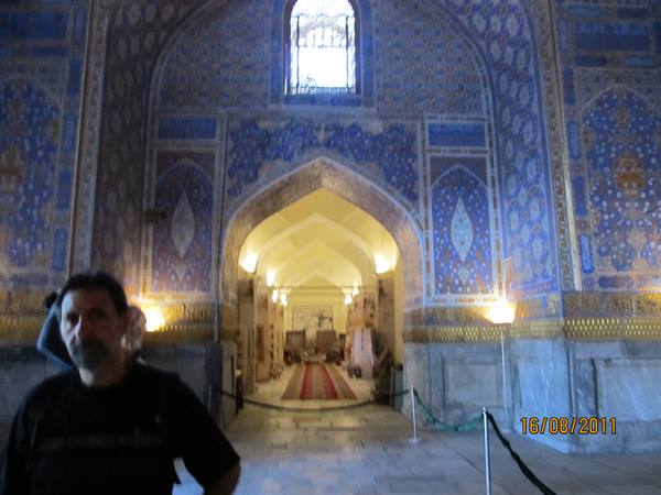 Man in front of hall with blue mosaic walls, arches and red carpet, Samarkand