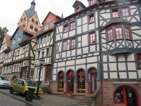 Half-timbered houses with blue beams and shops beneath a romanesque church tower