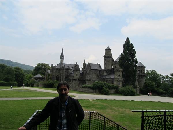 Man in front of Löwenburg castle, green lawn and stone towers