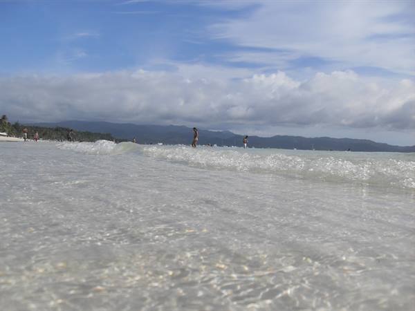 Clear shallow water on the beach, swimmers among waves and cloudy hills