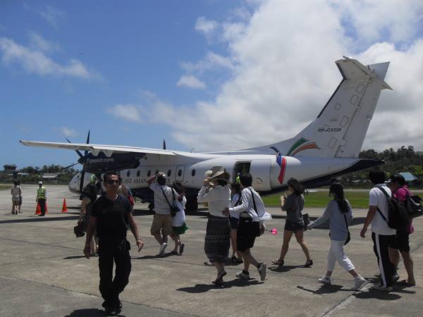 Passengers walk toward a white turboprop plane parked on the tarmac