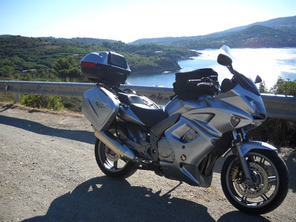 Silver Honda touring motorcycle with panniers parked on sunny coastal road above the sea