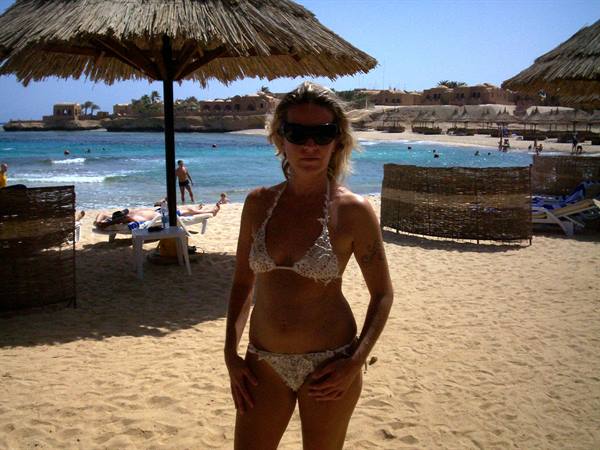 Woman in white bikini under straw umbrella on golden sand beach