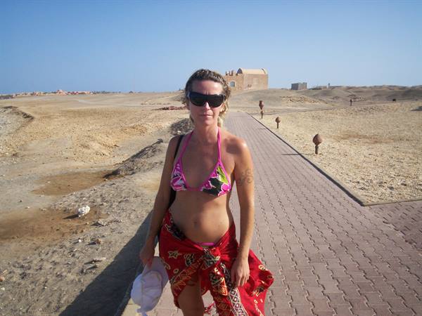 Woman in pink bikini and red sarong walks on brick path through desert