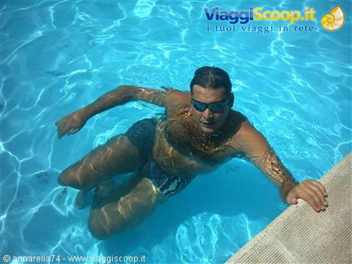 Man in sunglasses swimming in blue pool, hand on edge