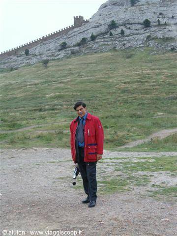 Man in red jacket with camera below ancient fortress walls on the hill