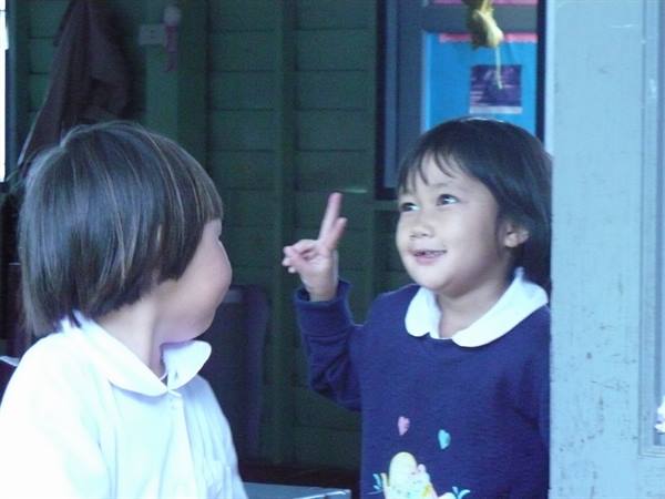 Smiling girl points finger at a friend in front of green wall