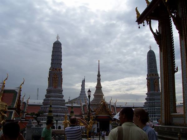 Tourists photograph the golden stupas of Wat Phra Kaew under a cloudy sky