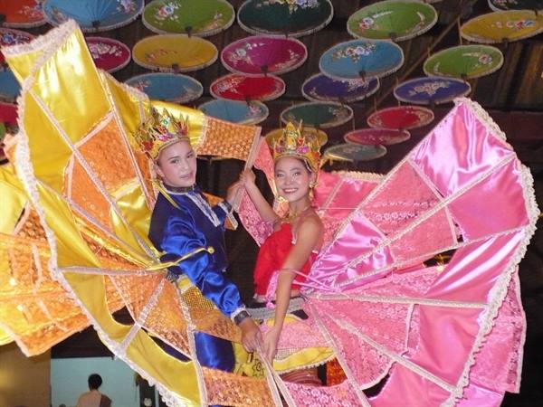Dancers in yellow and pink costumes under colorful hanging umbrellas