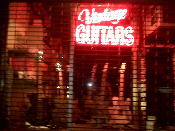 Red neon Vintage Guitars sign above guitars in a shop window at night