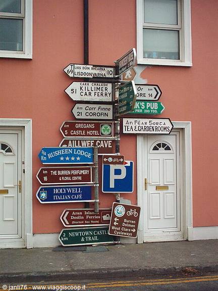 Crowded road signs on the pink wall of a house in Doolin