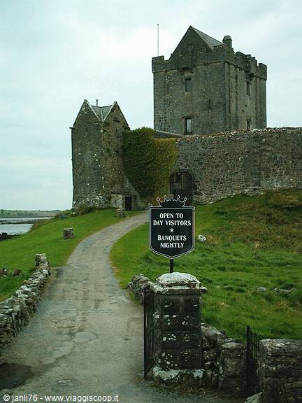 Dunguaire Castle stone tower with visitors sign, green grass and grey sky