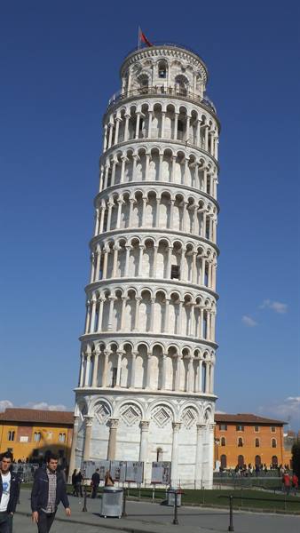 Tourists walk beneath the Leaning Tower of Pisa, white marble under blue sky