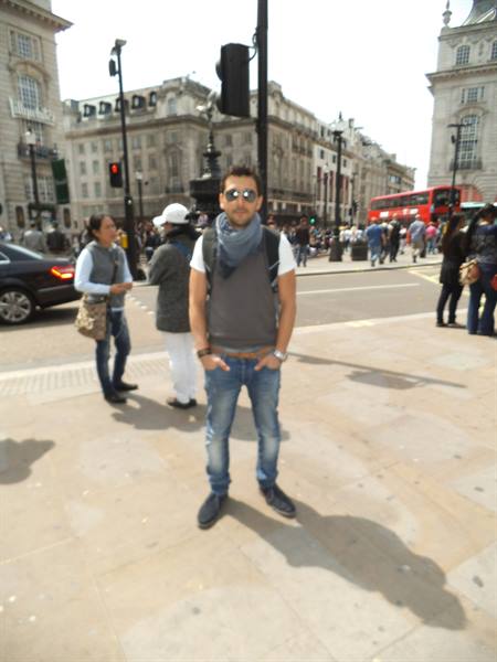 Tourist with scarf and backpack standing at Piccadilly Circus, London, red bus behind