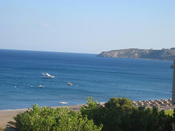 Boats anchored on blue sea in front of beach with umbrellas and rocky headland