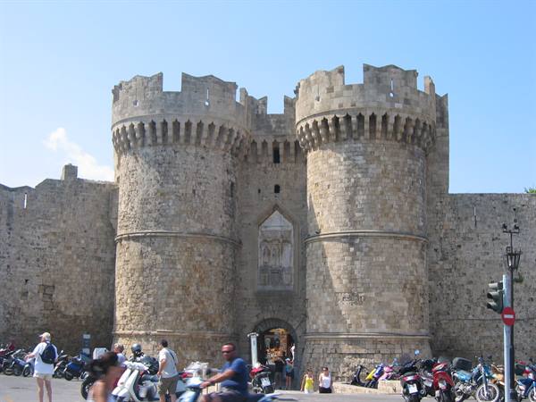 Medieval gate with two stone towers in Rhodes, tourists and scooters under the sun