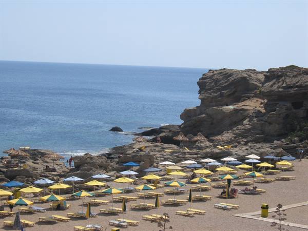 Beach with yellow umbrellas and sunbeds beneath rocky cliffs, blue sea