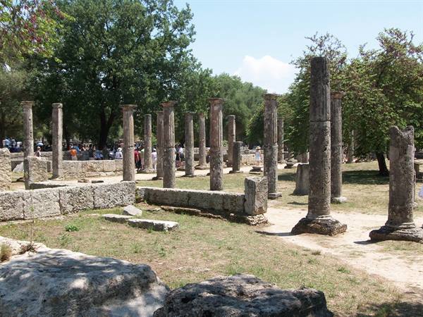 Weathered stone columns among trees and visitors at the ancient site of Olympia