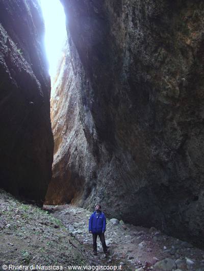 Hiker in blue jacket between tall rock walls of a narrow gorge