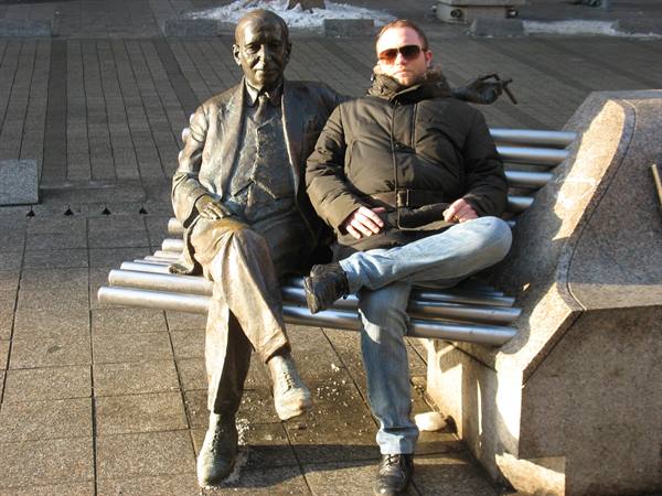 Tourist in sunglasses sitting next to a bronze statue on a bench