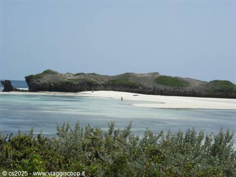 White sand beach with green rocky headland and turquoise water, people walking along shore
