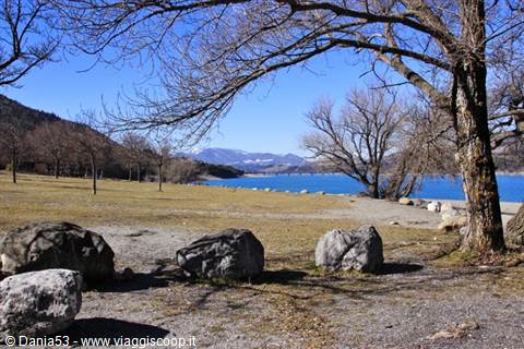 Bare trees and boulders on the grass by the blue winter lake