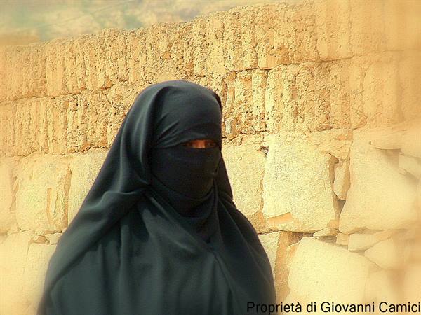 Woman in black niqab walks past an ancient stone wall