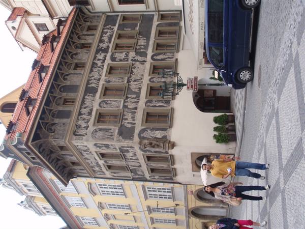 Tourists walk past a painted sgraffito facade in Prague's Old Town Square