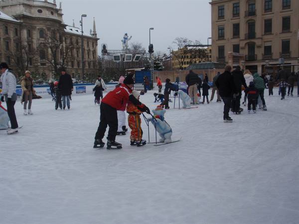 Outdoor city ice rink, adults helping children skate in winter clothes