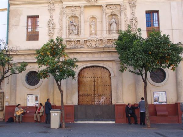 Baroque church facade with wooden portal, people seated beneath orange trees