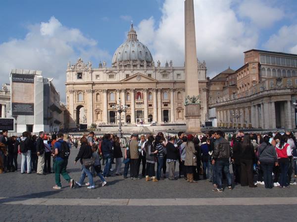 Tourists in St. Peter's Square before the basilica and obelisk, cloudy sky
