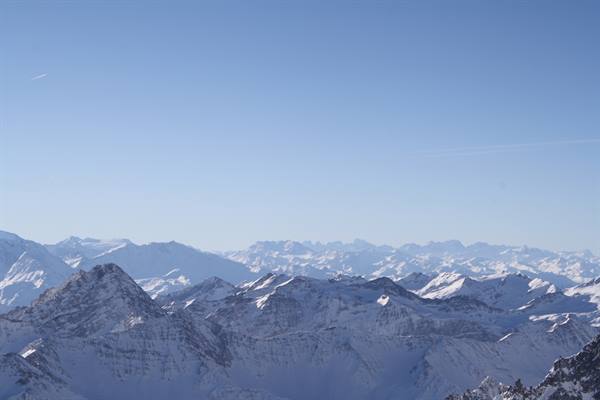 Snow-covered peaks stretching far under a clear pale blue sky