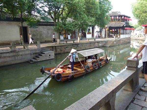 Wooden canopy boat rowed along Tongli canal past whitewashed houses and lanterns
