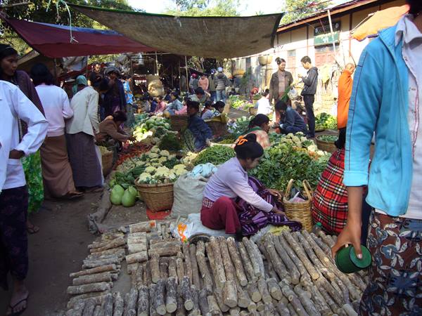 Open-air market with vegetable vendors and wooden stalks in the foreground