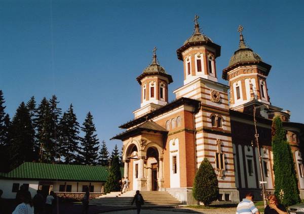 Sinaia Monastery church with ochre towers and visitors under a blue sky
