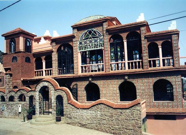Brick and stone building with arches, stained glass windows, and wavy wall under blue sky