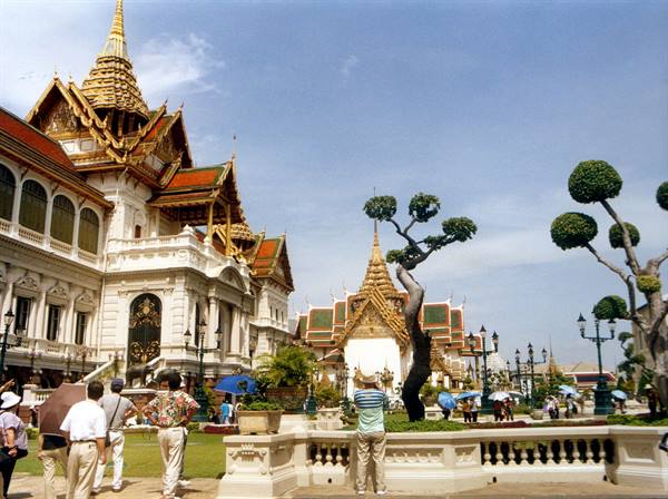 Tourists with umbrellas walk among golden pavilions at Bangkok's Grand Palace