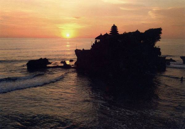Tanah Lot temple silhouetted on rocky outcrop, waves and orange sun