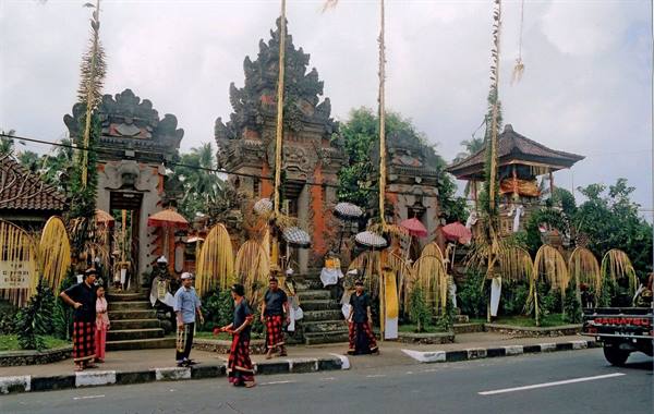 Balinese temple with bamboo penjor poles, people in traditional dress