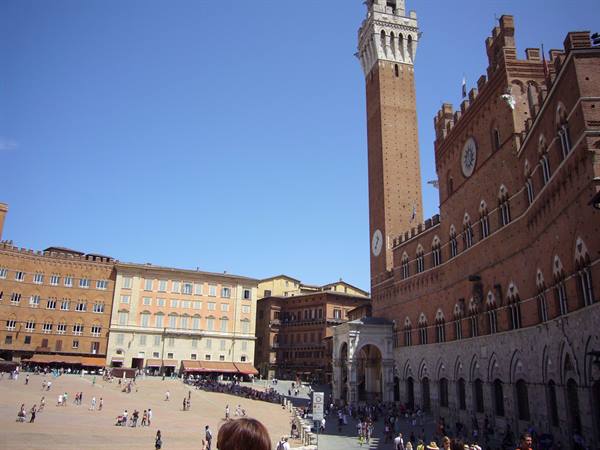 Tourists in Piazza del Campo, Siena, beneath the Torre del Mangia in morning light