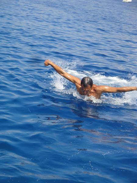 Man swims butterfly in blue sea, arms wide, splashing water