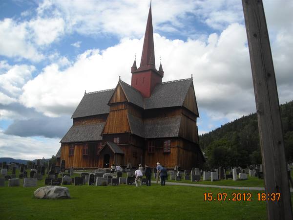Ringebu stave church, dark wooden shingles over graves under cloudy sky